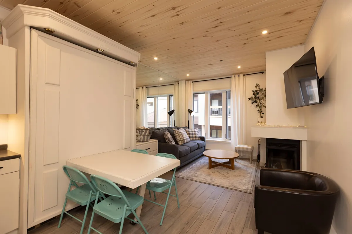 An open-concept living and dining space, featuring a comfortable sofa, a dining table set for sharing meals, a television, and a fireplace. Large windows frame scenic views, while the layout encourages both relaxation and group gatherings.