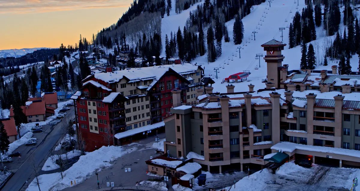 A scenic winter view of Purgatory Village Plaza featuring snow-covered streets, charming resort buildings, ski lifts, and majestic mountain slopes. The scene captures the inviting ambiance and adventure-filled surroundings of the resort area.