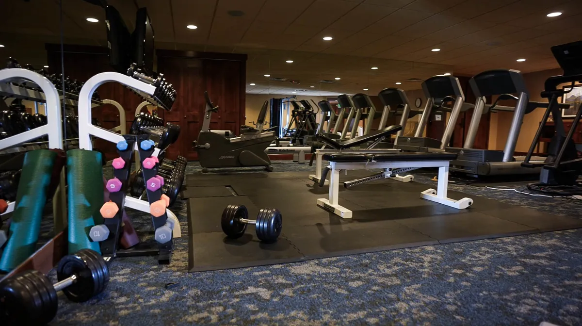 A bright, modern fitness center featuring an array of equipment, including dumbbells, treadmills, exercise machines, and a weight bench. The space is filled with natural light and offers ample room for both individual and group workouts, creating an energetic atmosphere ideal for staying active during extended stays.