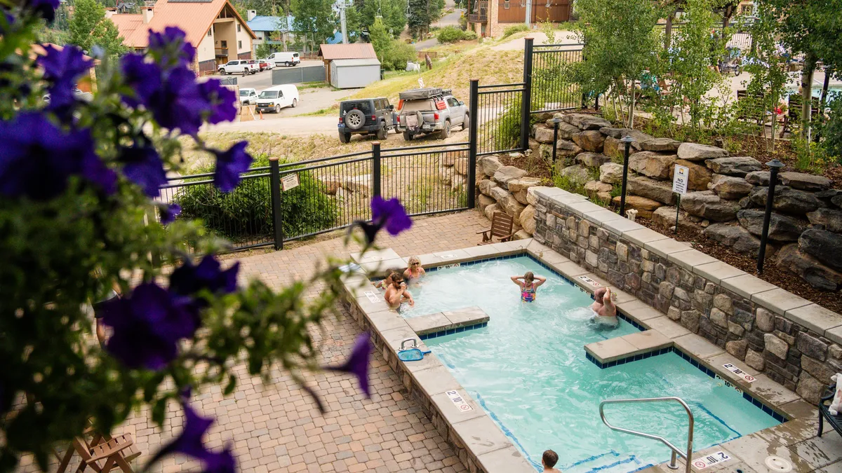 A welcoming outdoor swimming pool surrounded by colorful flowers and people enjoying the water. The scene conveys relaxation, socializing, and the laid-back side of resort living, with hints of both daytime and evening enjoyment.