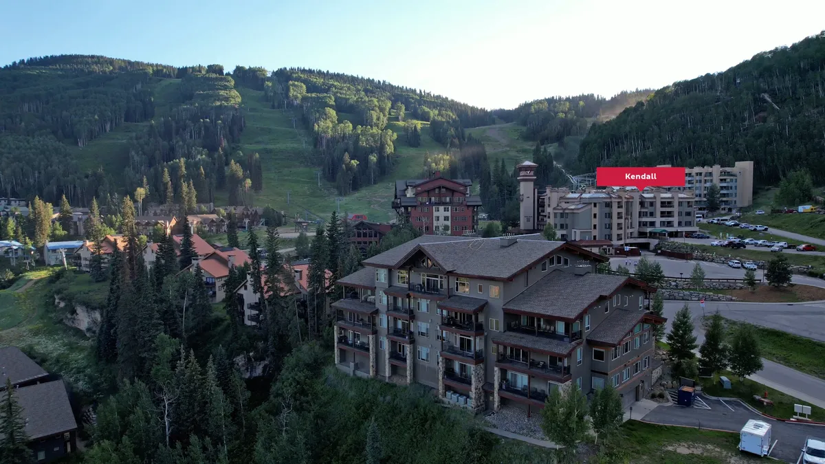 An exterior view of the resort area, highlighting the mountain landscape, ski resort buildings, tree lines, and a visible parking area. The garage parking is conveniently situated near both the mountains and resort amenities.