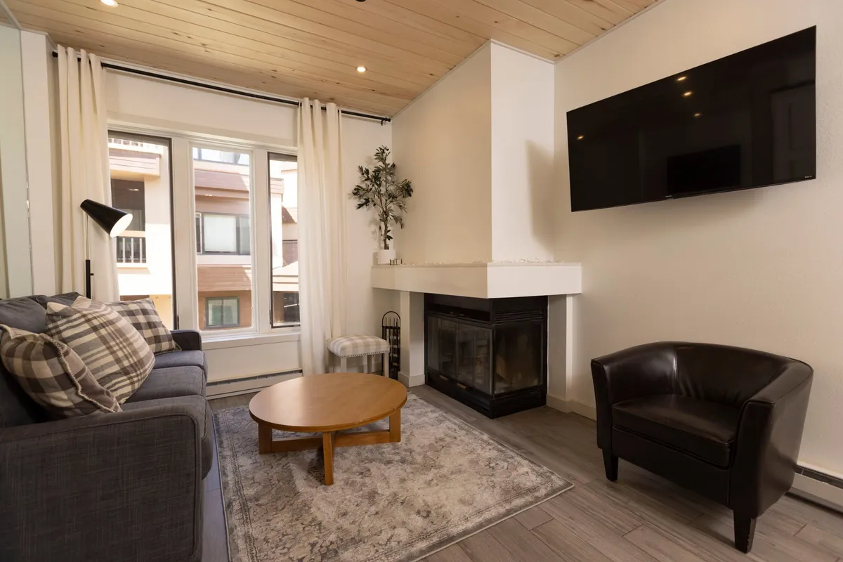 A cozy interior space featuring a comfortable sofa positioned in front of a stone fireplace, a coffee table, and a wall-mounted television. The ambiance is inviting, perfect for relaxing after a productive day or enjoying downtime while staying connected with modern amenities.