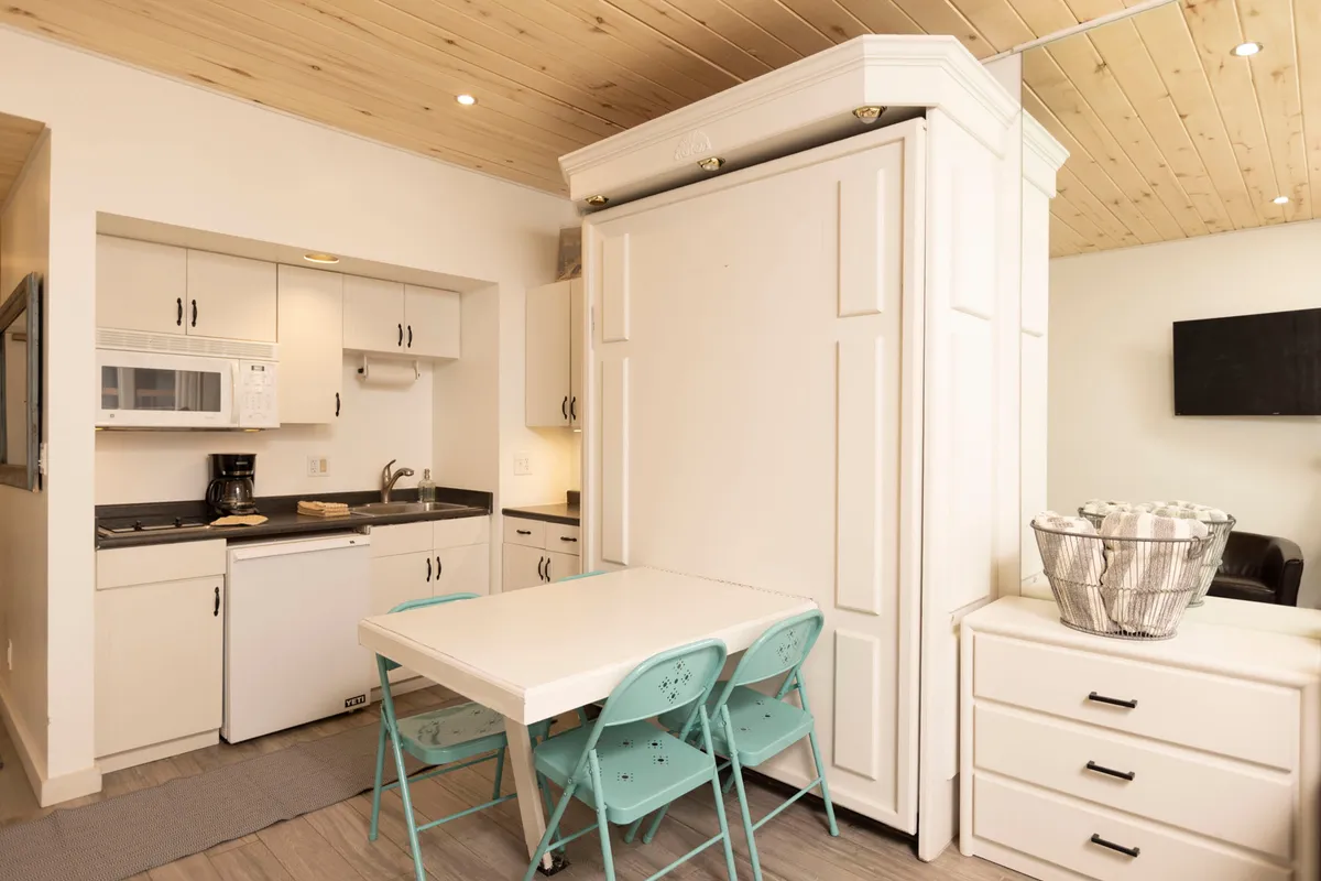 A stylish, fully equipped kitchenette with a folding table and turquoise chairs, complemented by modern white cabinetry. The setup is ideal for prepping meals, hosting intimate dinners, or enjoying morning routines with friends and family.